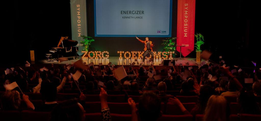 presentator op podium met verlichte letters Zorg en Toekomst