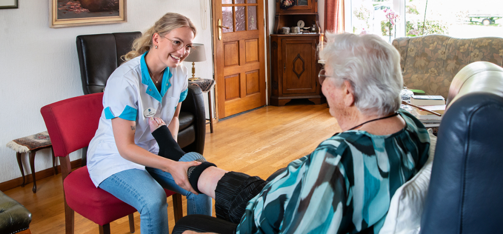 Thuiszorgmedewerker van Omring trekt een steunkous aan bij iemand thuis.