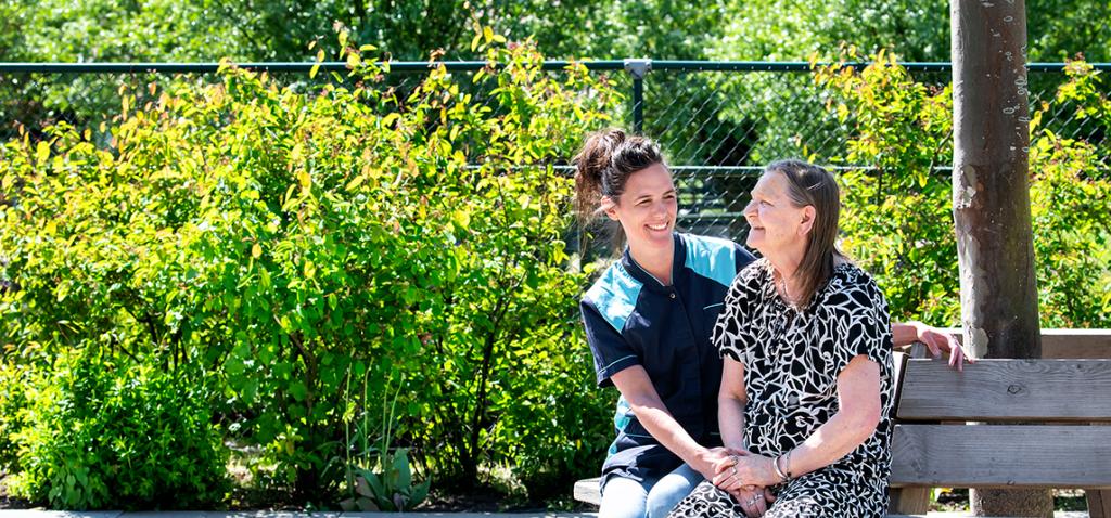 Een medewerker van Omring zit samen met een bewoner op een bankje in de tuin.