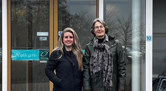 Op de foto staan vrijwilligers coördinator Vivian en vrijwilliger Anneke voor de deur van Omringlocatie De Watermolen in Abbekerk.