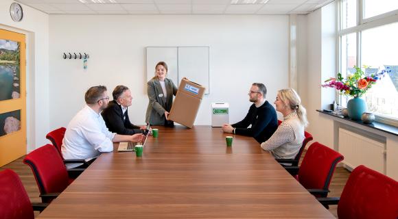 Een bespreking van het Green Team van Omringlocatie Nicolaas. Eén medewerker houdt een kartonnen doos omhoog.