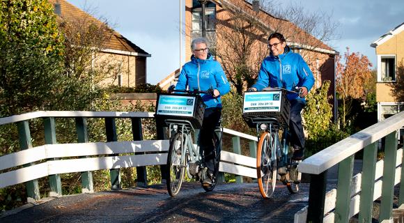 Twee thuiszorgmedewerkers van Omring fietsen over een brug.