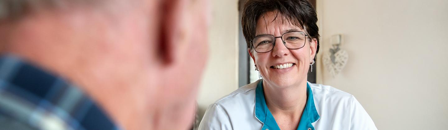 Verpleegkundige zit aan de keukentafel en is in gesprek met een meneer.