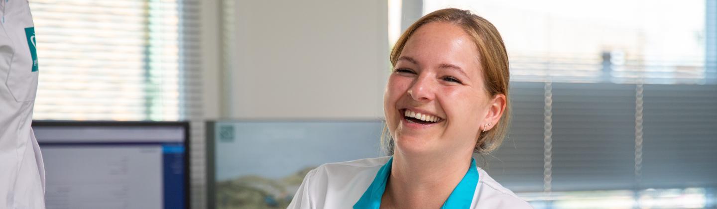 Medewerker van het thuiszorgteam zit op kantoor en is lachend in gesprek met haar collega's.,