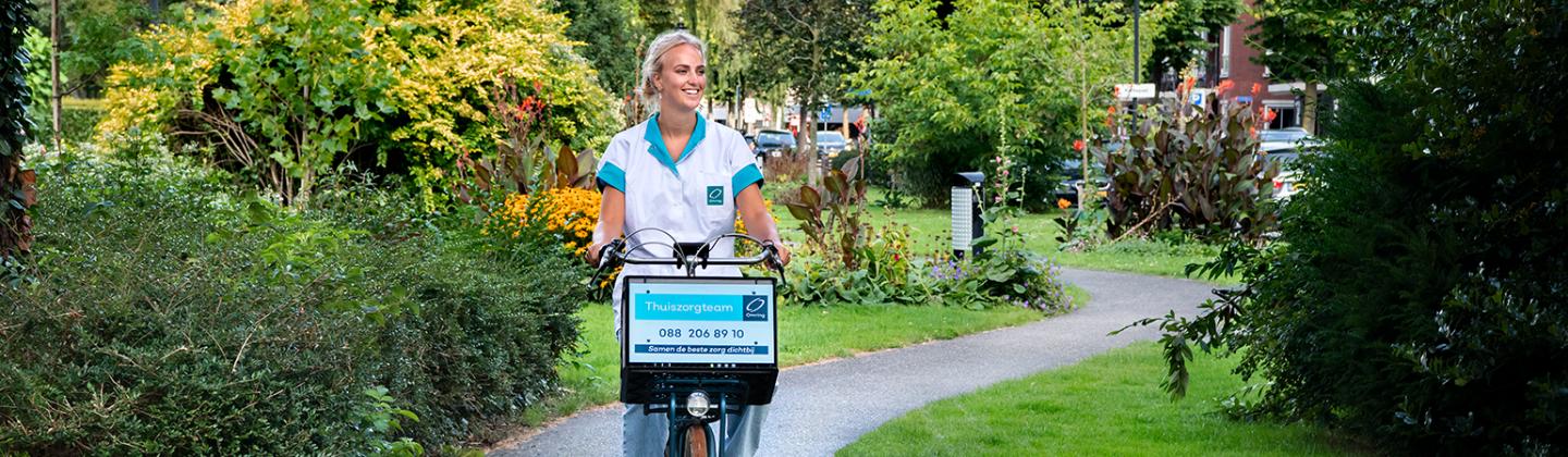 Medewerker van de thuiszorg fietst door het park.