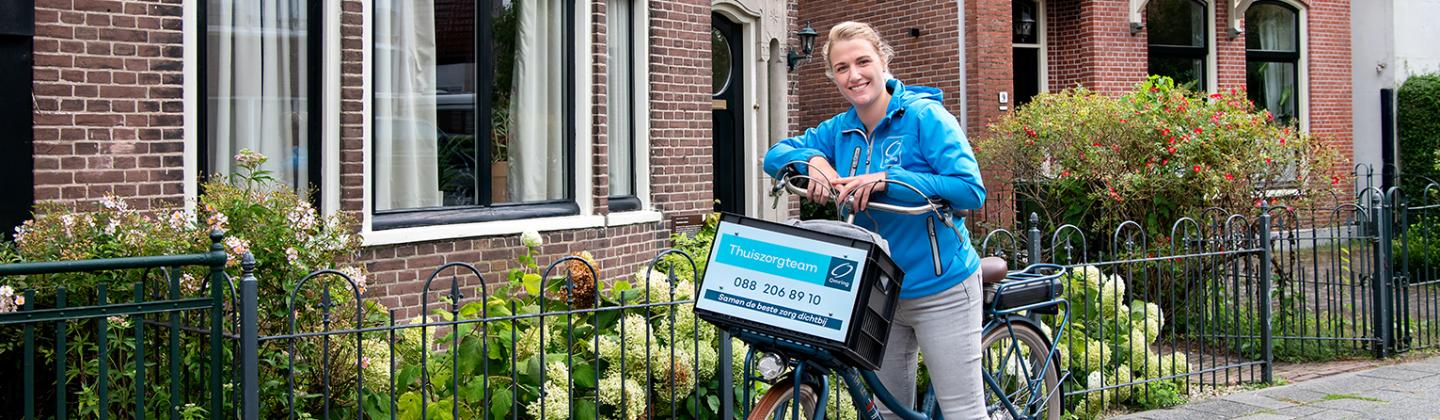 Medewerker van de thuiszorg leunt op haar fietsstuur en poseert.