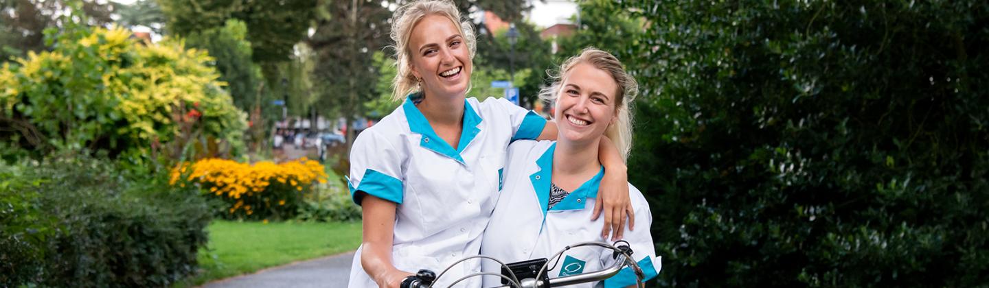 Medewerkers van de thuiszorg lachen arm in arm naar de camera.