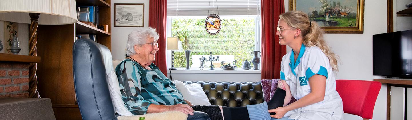 Medewerker van de thuiszorg van Omring helpt een cliënt thuis met steunkousen.
