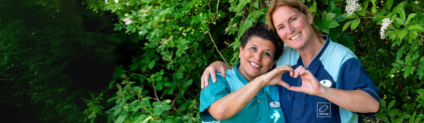 Twee medewerkers van Omring staan arm in arm en maken een hartje van hun handen.