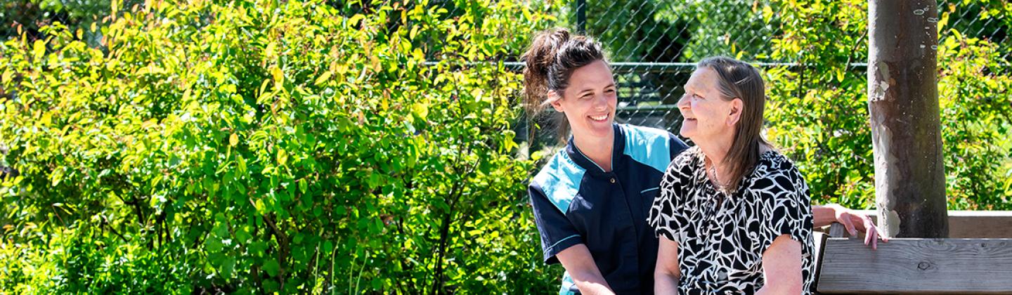 Een medewerker van Omring zit samen met een bewoner op een bankje in de tuin.
