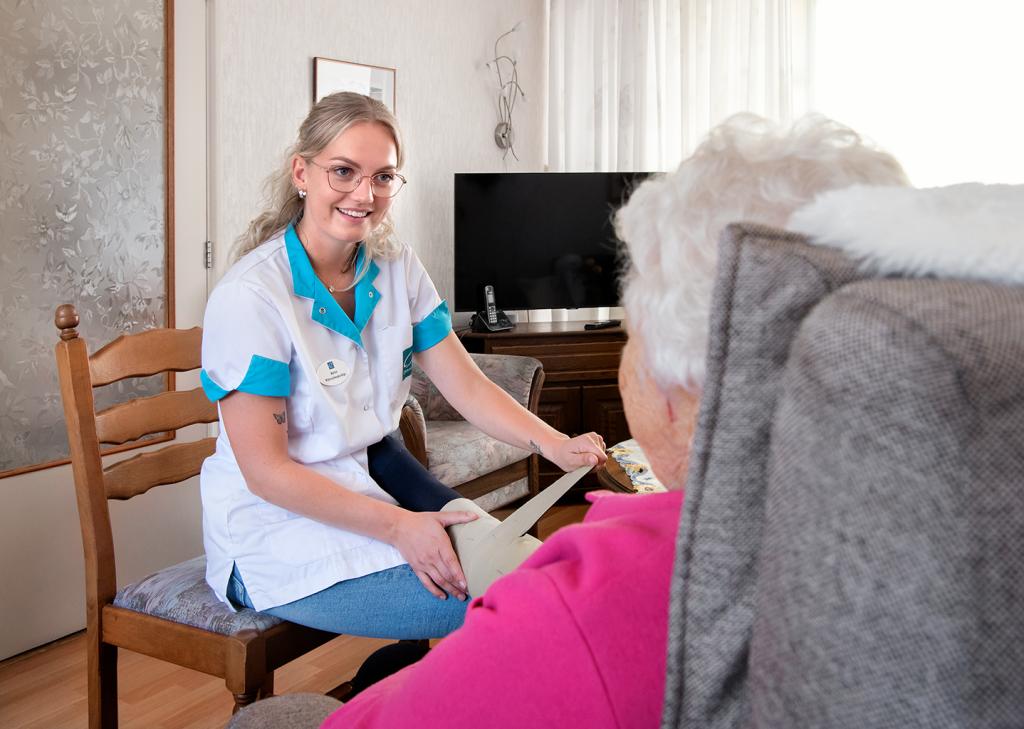 Omringmedewerker verbindt het been van een oudere dame in de woonkamer.