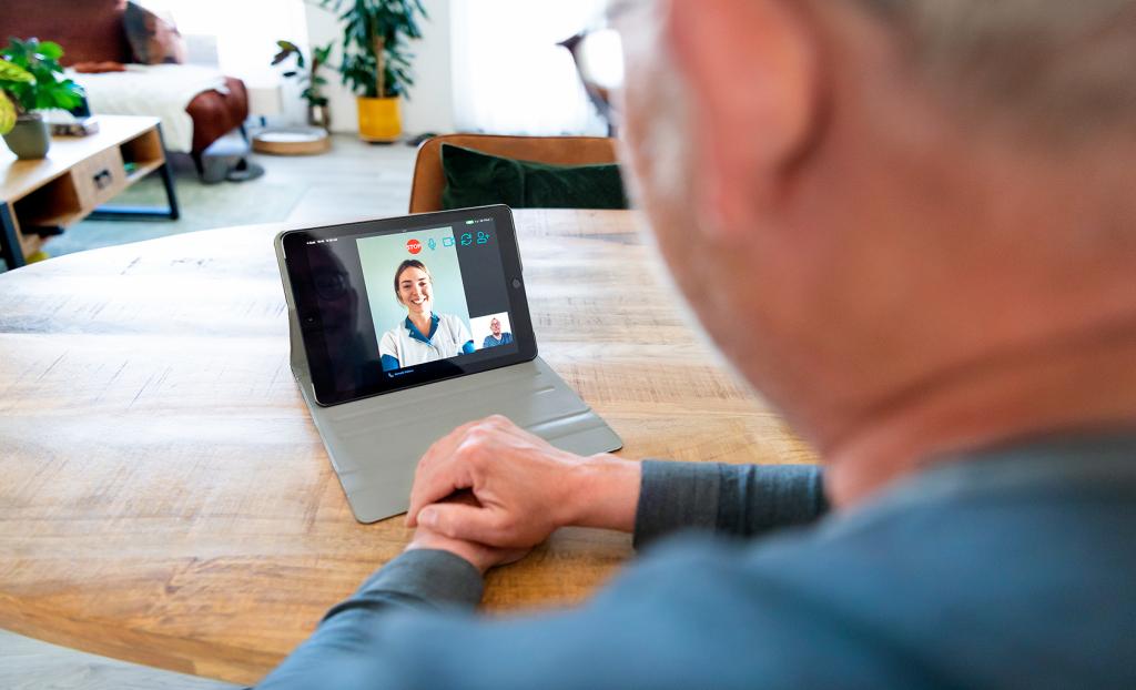 Een meneer praat met een verpleegkundige via een iPad.