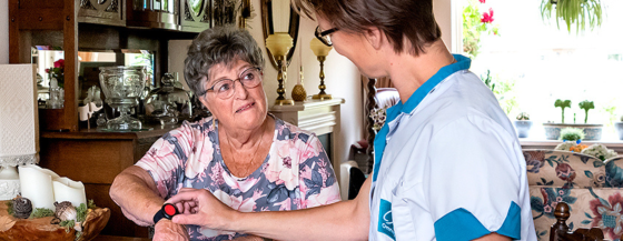 Een verpleegkundige van Omring geeft uitleg over de alarmknop van de personenalarmering, die een mevrouw als armband draagt.