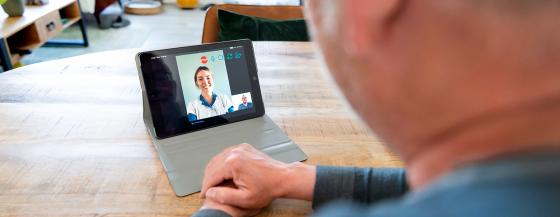 Een meneer praat met een verpleegkundige via een iPad.