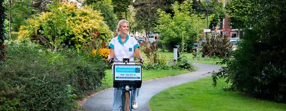 Medewerker van de thuiszorg fietst door het park.