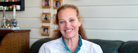 Medewerker van de Omring thuiszorg poseert voor de camera. Ze lacht en zit op de bank in de woonkamer van een cliënt.