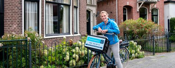 Medewerker van de thuiszorg leunt op haar fietsstuur en poseert.