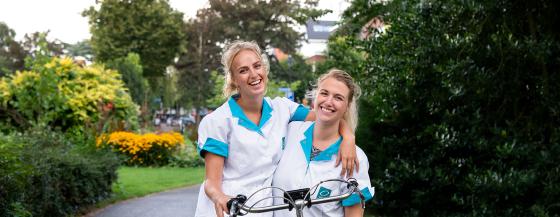 Medewerkers van de thuiszorg lachen arm in arm naar de camera.