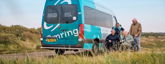 Medewerker, mantelzorger en twee cliënten van Omring in een rolstoel staan met z'n vieren bij elkaar in de duinen van Den Helder.