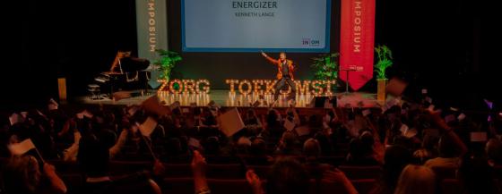 presentator op podium met verlichte letters Zorg en Toekomst