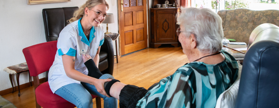 Thuiszorgmedewerker van Omring trekt een steunkous aan bij iemand thuis.