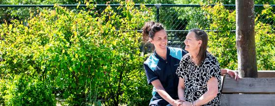 Een medewerker van Omring zit samen met een bewoner op een bankje in de tuin.
